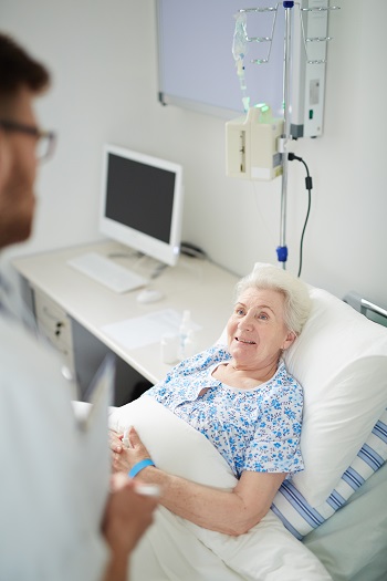 Senior patient lying in bed while talking to her doctor.