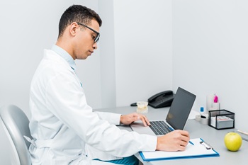 Clinician sitting at desk with laptop taking notes.  Office phone and supplies in the background.