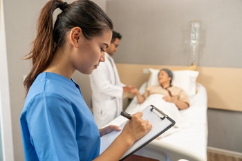 Doctor documents personal information in patient's chart at their bedside. 